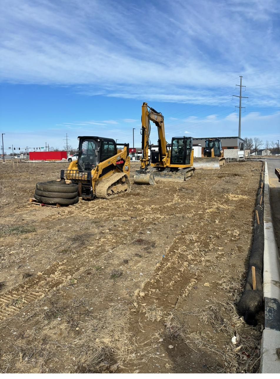 Track loader and excavator staged on a jobsite at sunrise