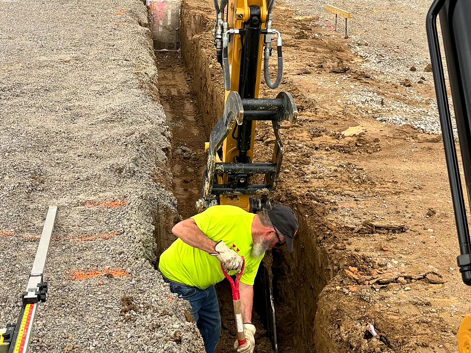Crew member verifying grade in a footing trench beside the excavator